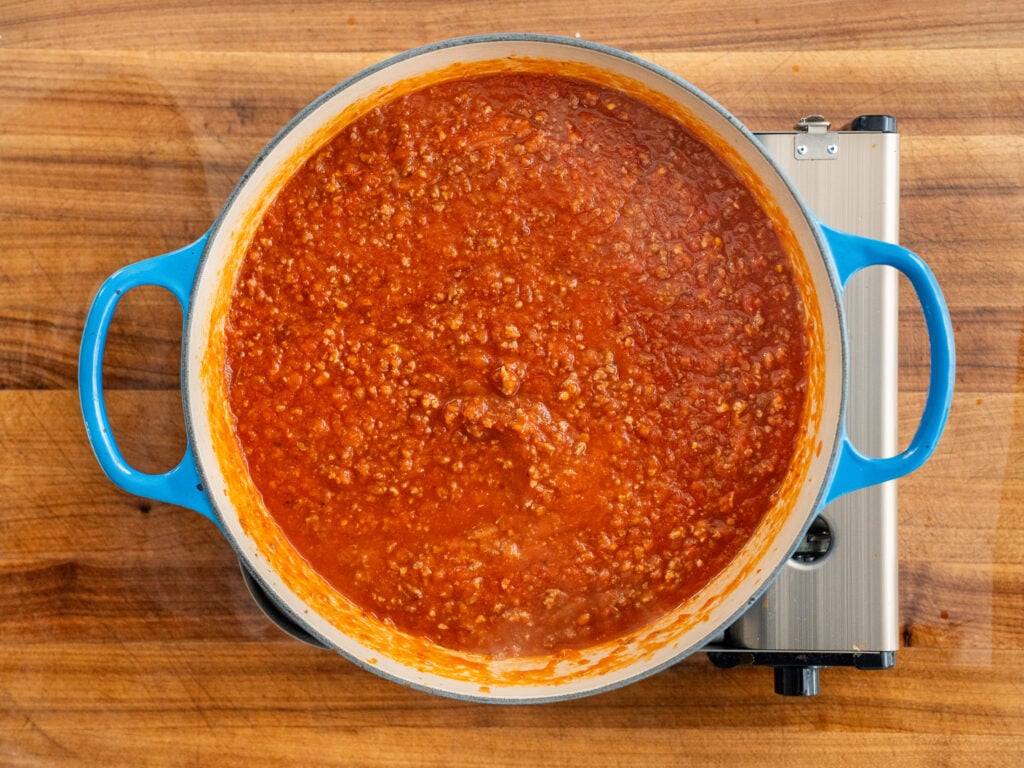 simmering tomato meat sauce in blue dutch oven