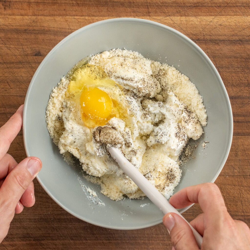 stirring ricotta mixture in grey bowl with white spatula