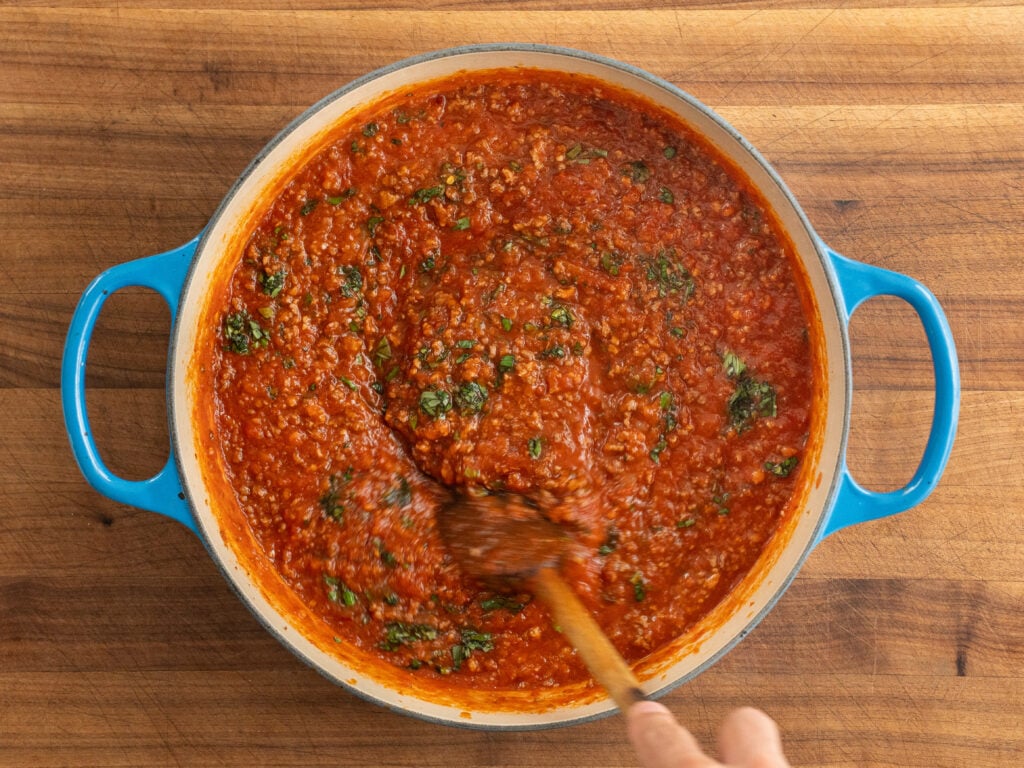 wooden spoon stirs basil into meat sauce