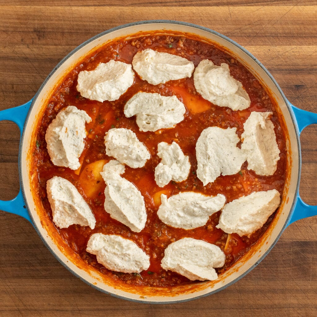 blue dutch oven filled with meat sauce topped with dollops of ricotta mixture