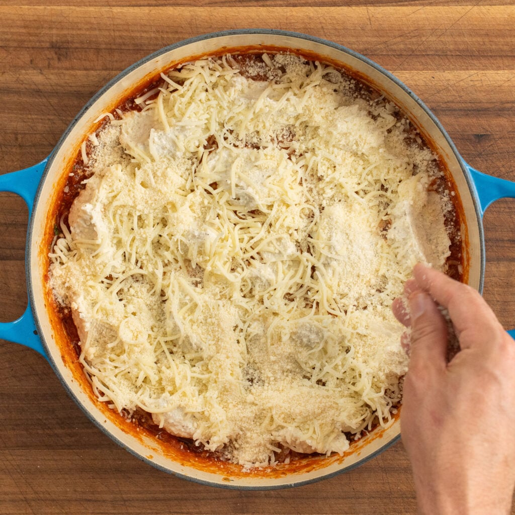 hand sprinkles parmesan on top of pre-baked pot of one-pot lasagna