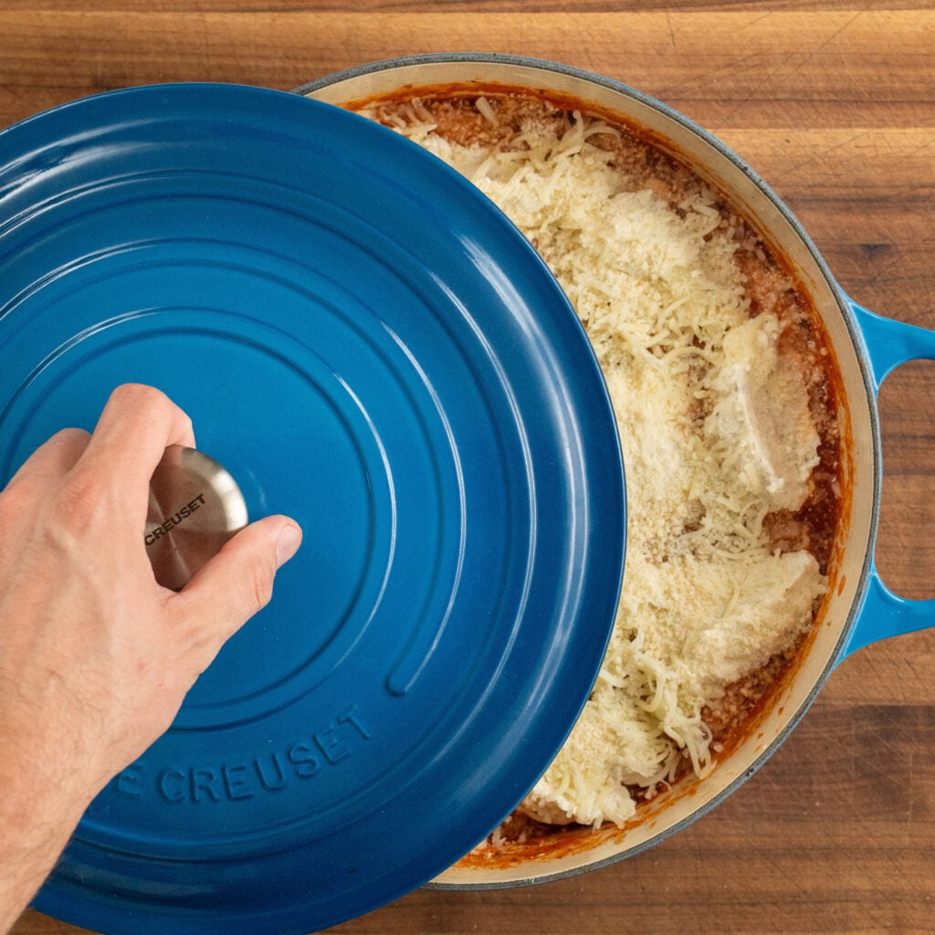 covering blue dutch oven filled with one pot lasagna with lid