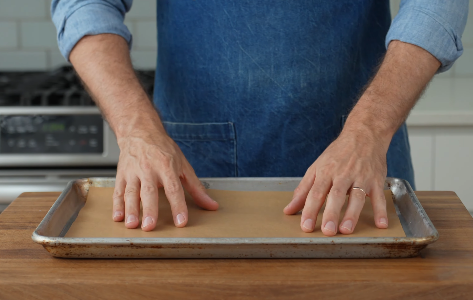 man in blue apron with hands placing sheet of parchment paper on sheet tray