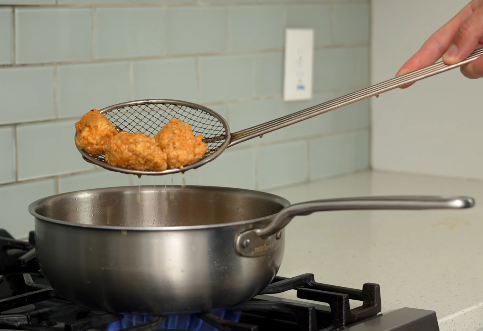 hadn't pulling fried chicken nuggets out of a pot of oil with spider strainer