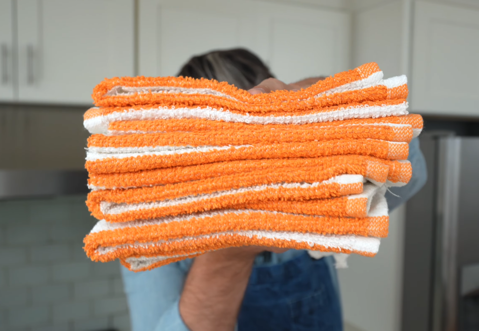 man in blue apron holding stack of orange and white towels