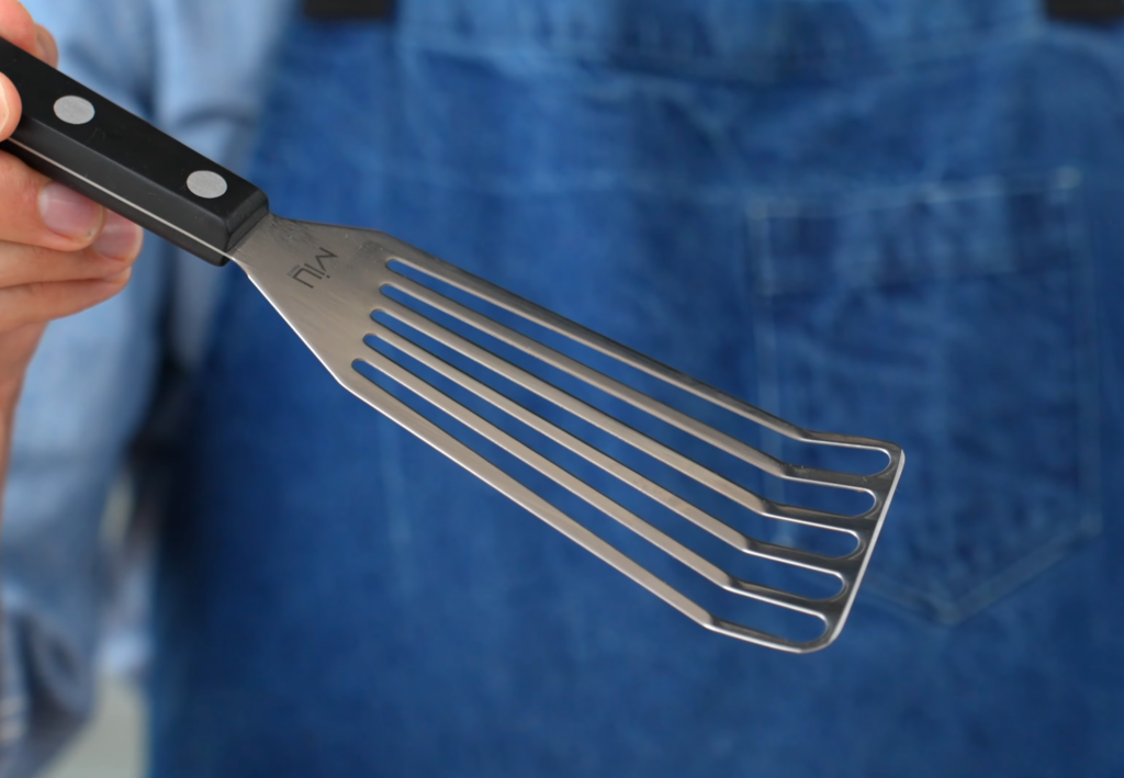 hand holding metal spatula with black handle in front of blue apron