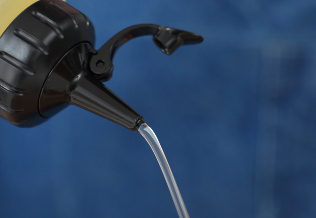 oil streaming out of black tip squeeze bottle in front of blue blurry background