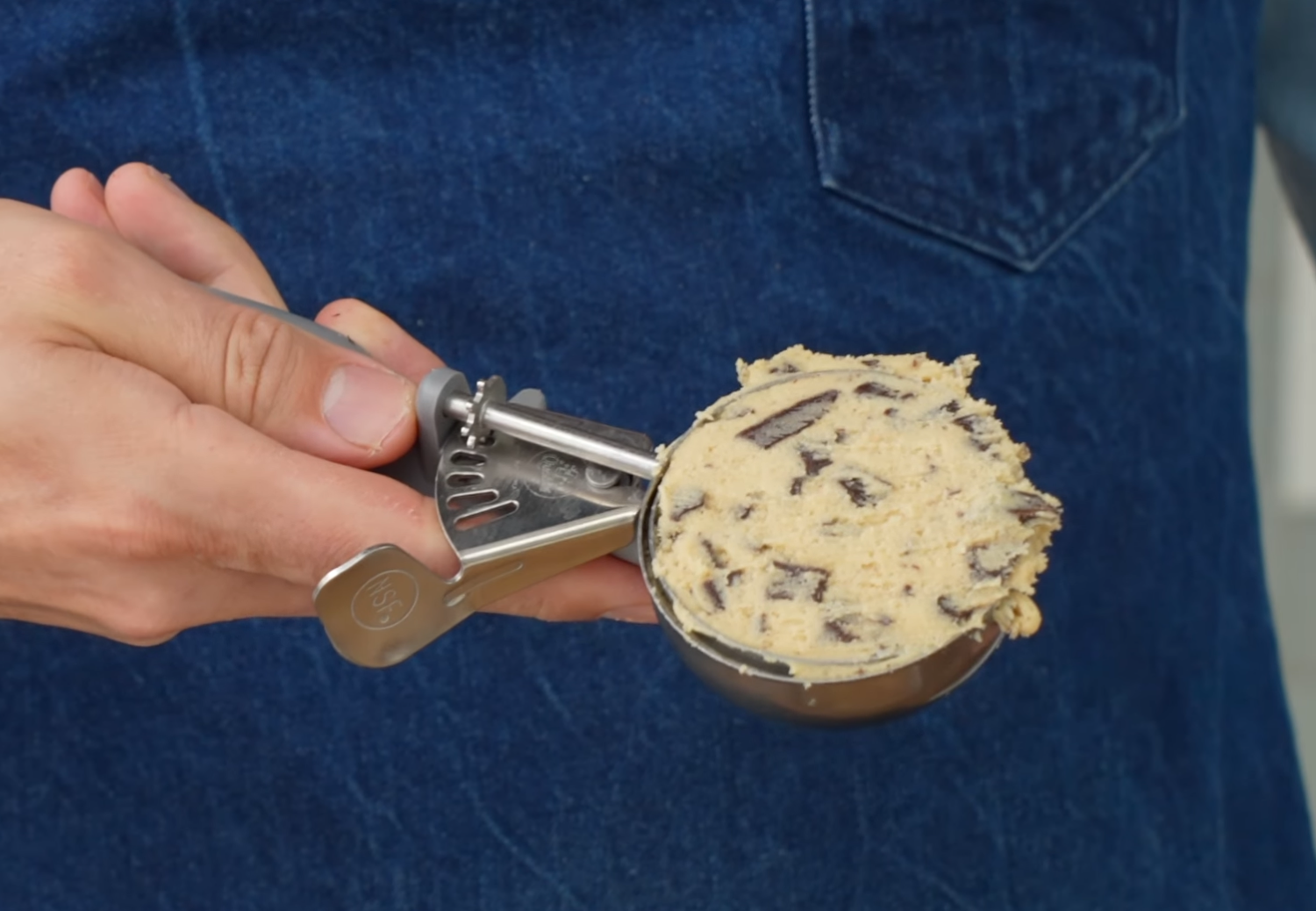 man in blue apron holding silver 4oz scoop with cookie dough
