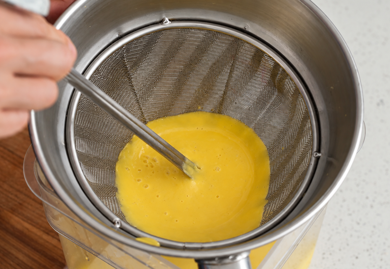 metal ladle pushing yellow soup through fine mesh strainer
