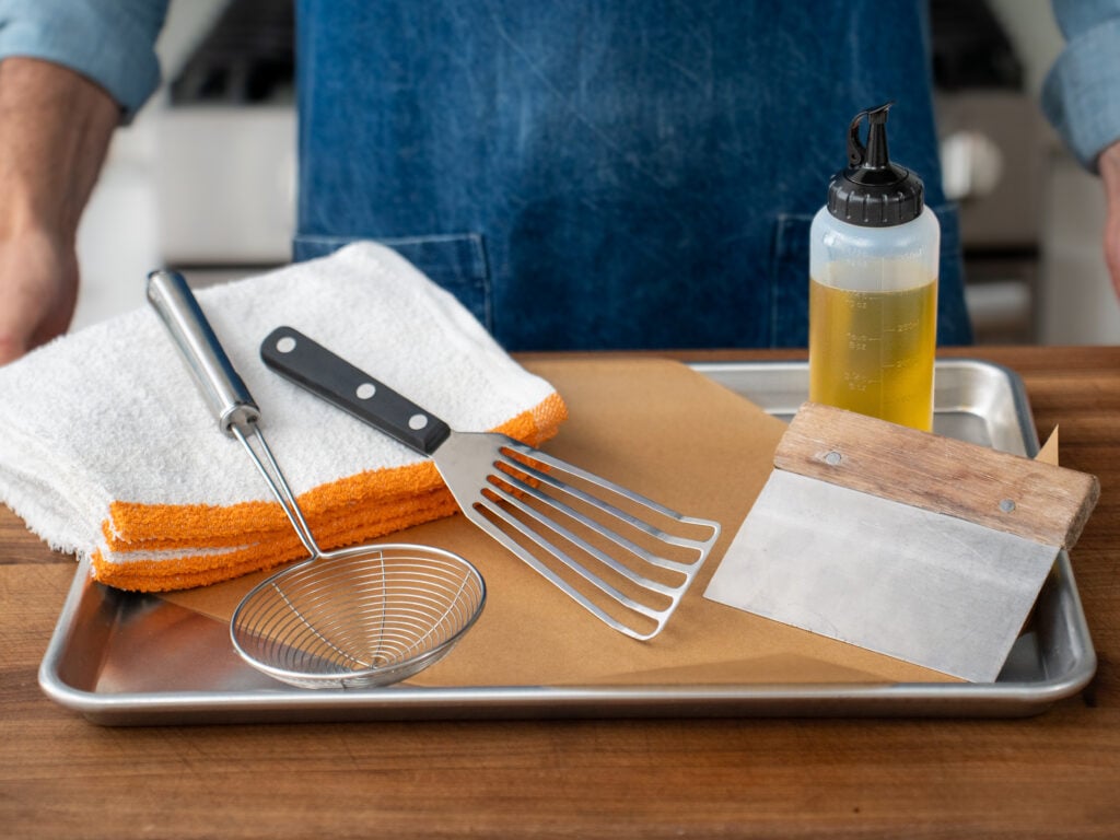 towels, strainer, spatula, bench scraper and squeeze bottle displayed on metal quarter sheet pan