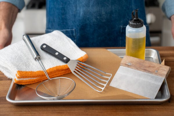 towels, strainer, spatula, bench scraper and squeeze bottle displayed on metal quarter sheet pan