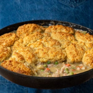 man in blue apron holding cast iron pan full of drop biscuit chicken pot pie